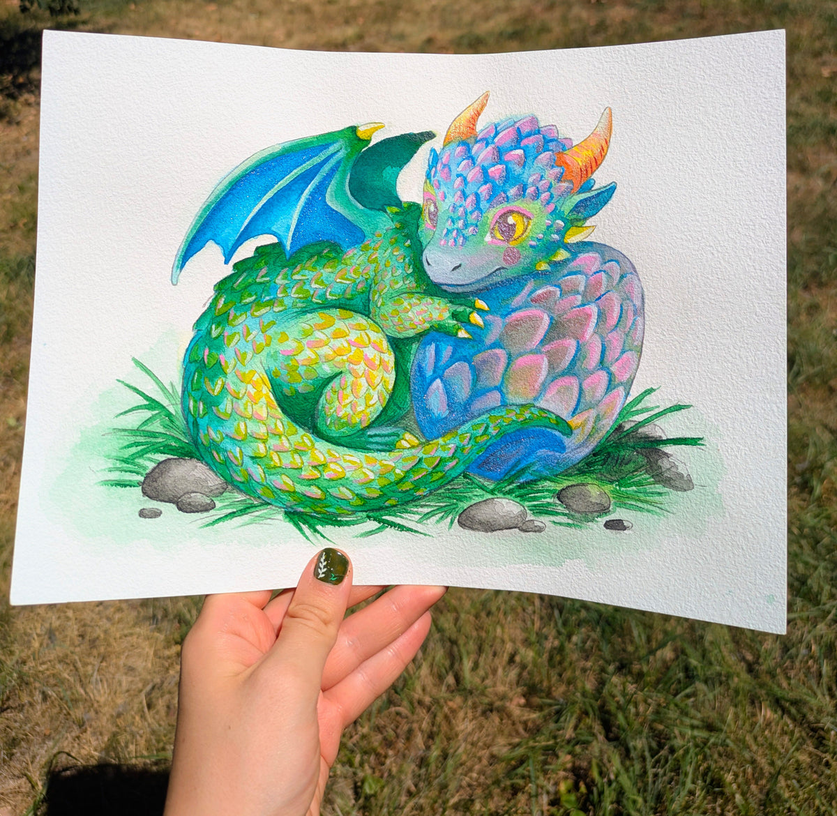 A hand holding a finished watercolor dragon painting